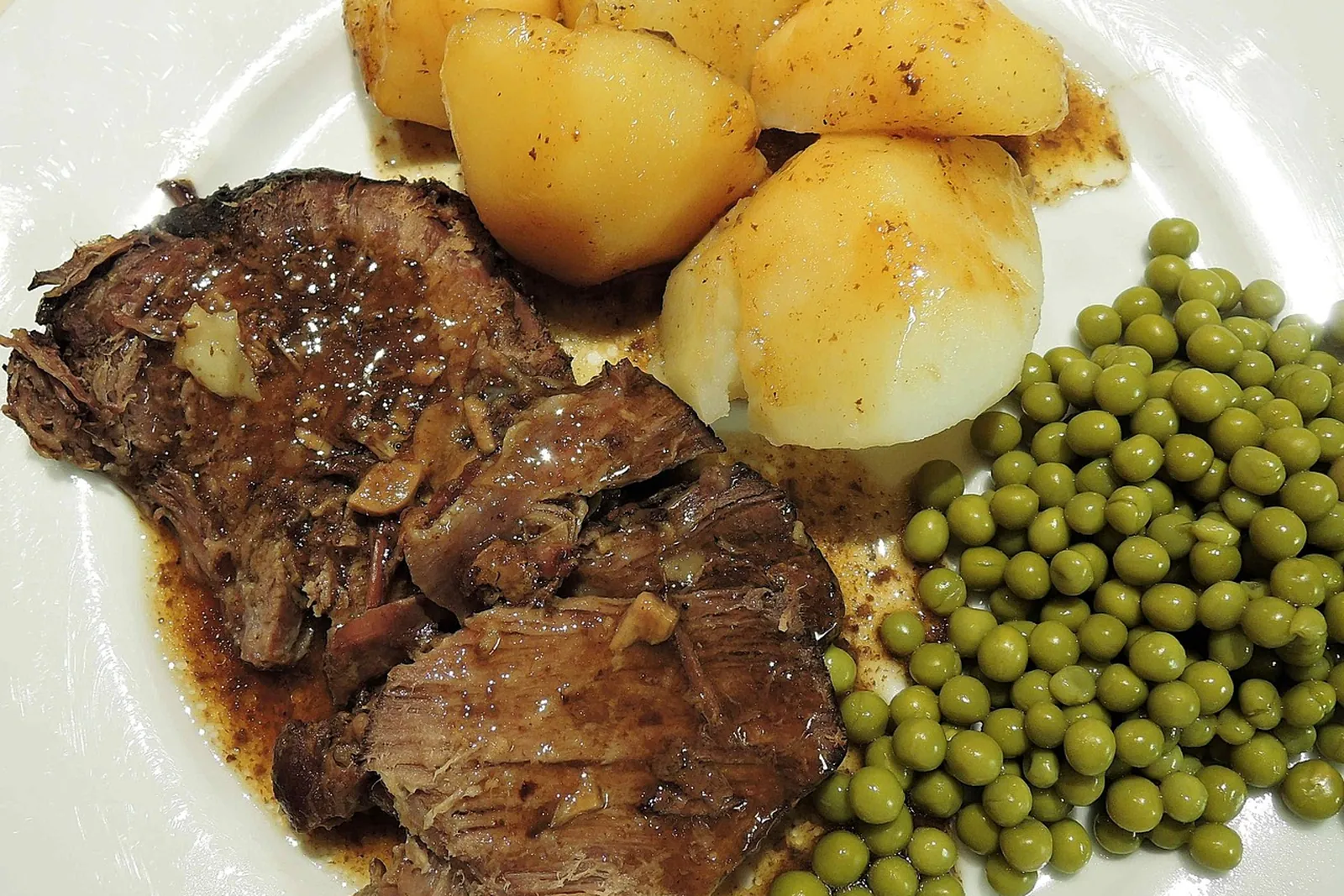 Pot roast with potatoes and peas on a white plate